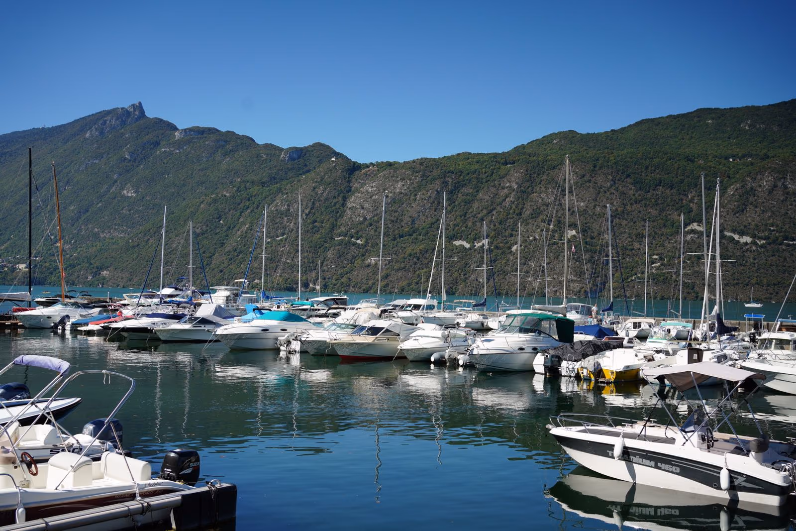 Voiliers et bateaux à moteur amarrés au port d’Aix-les-Bains, sous la crête boisée qui borde le lac du Bourget.