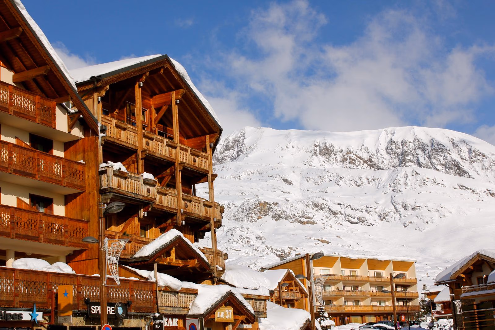Chalets en bois sous la neige fraîche, une face de montagne dénudée s’élevant à l’arrière.