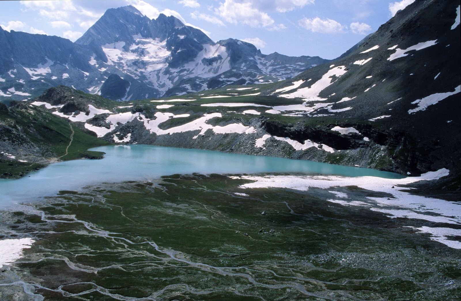 Un lac glaciaire turquoise et un alpage strié de neige sous des sommets rocheux, en Vanoise au-dessus de Pralognan.