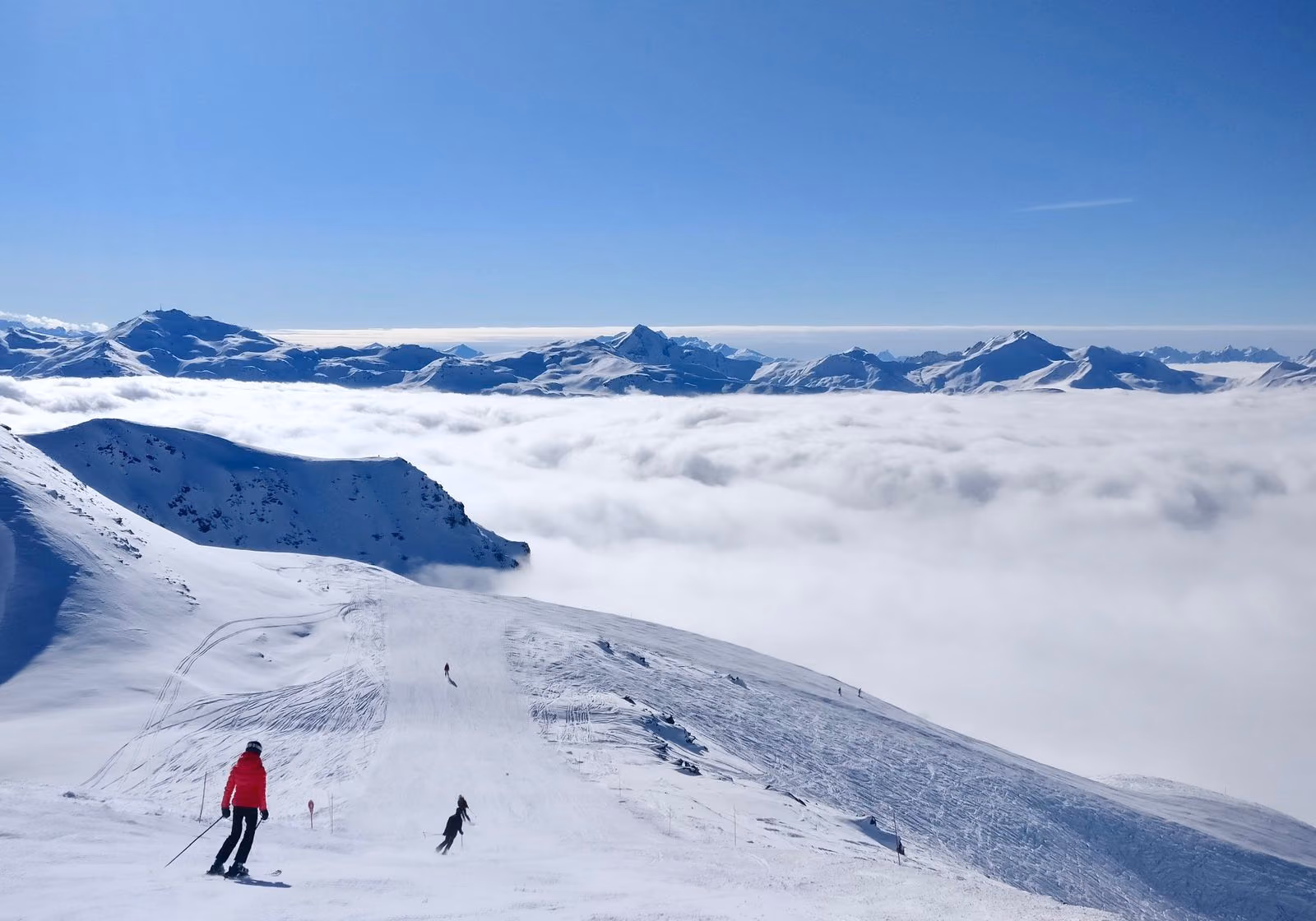Skieurs sur une piste d’altitude à Val Thorens, dominant une mer de nuages et des sommets lointains.
